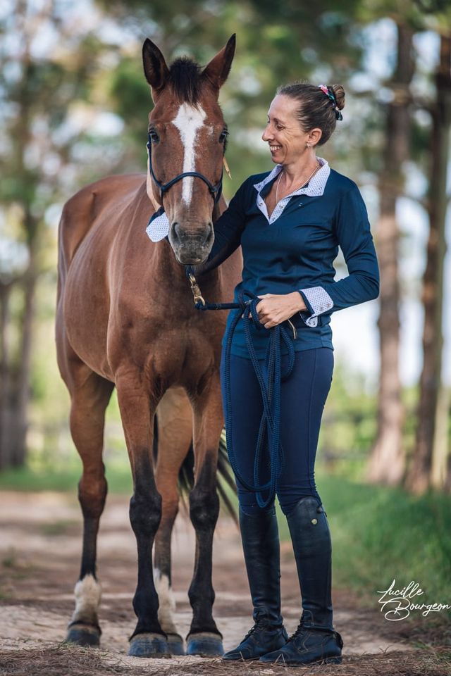 Cavalière souriante aux côtés de son cheval sur une allée ombragée