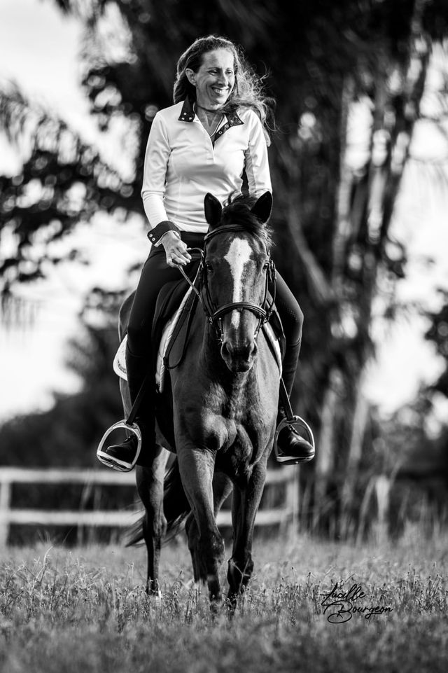 Portrait noir et blanc d'une cavalière souriante avançant à cheval